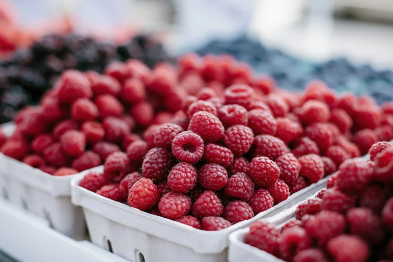 Fresh raspberries piled in white cardboard containers at a market stall