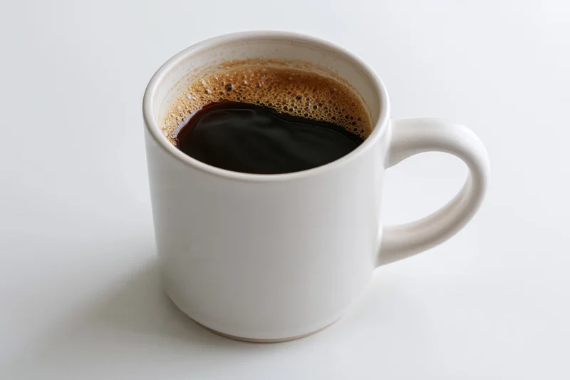 Plain white ceramic mug filled with black coffee showing crema