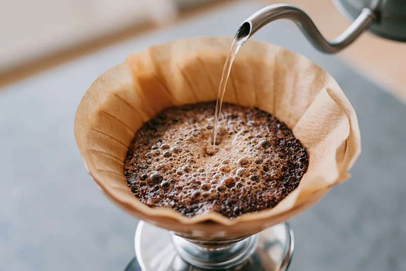 Water being poured over coffee grounds in a paper filter on a pour-over dripper