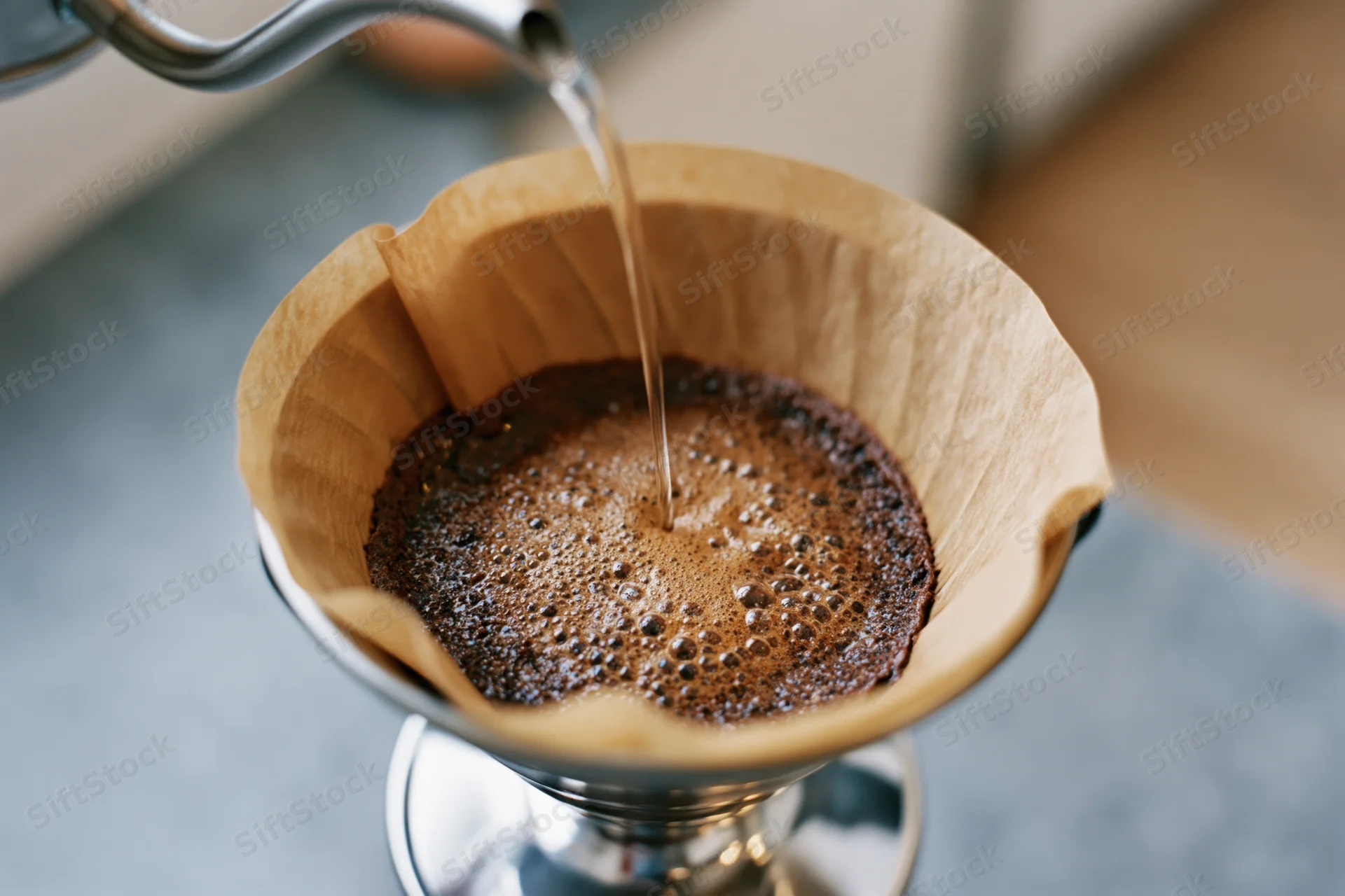 Water poured into a paper filter over coffee grounds in a metal dripper on a countertop