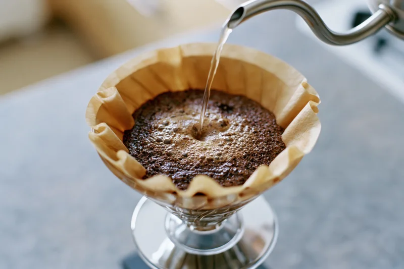 Water being poured into a paper filter over coffee grounds in a glass pour-over dripper on a countertop