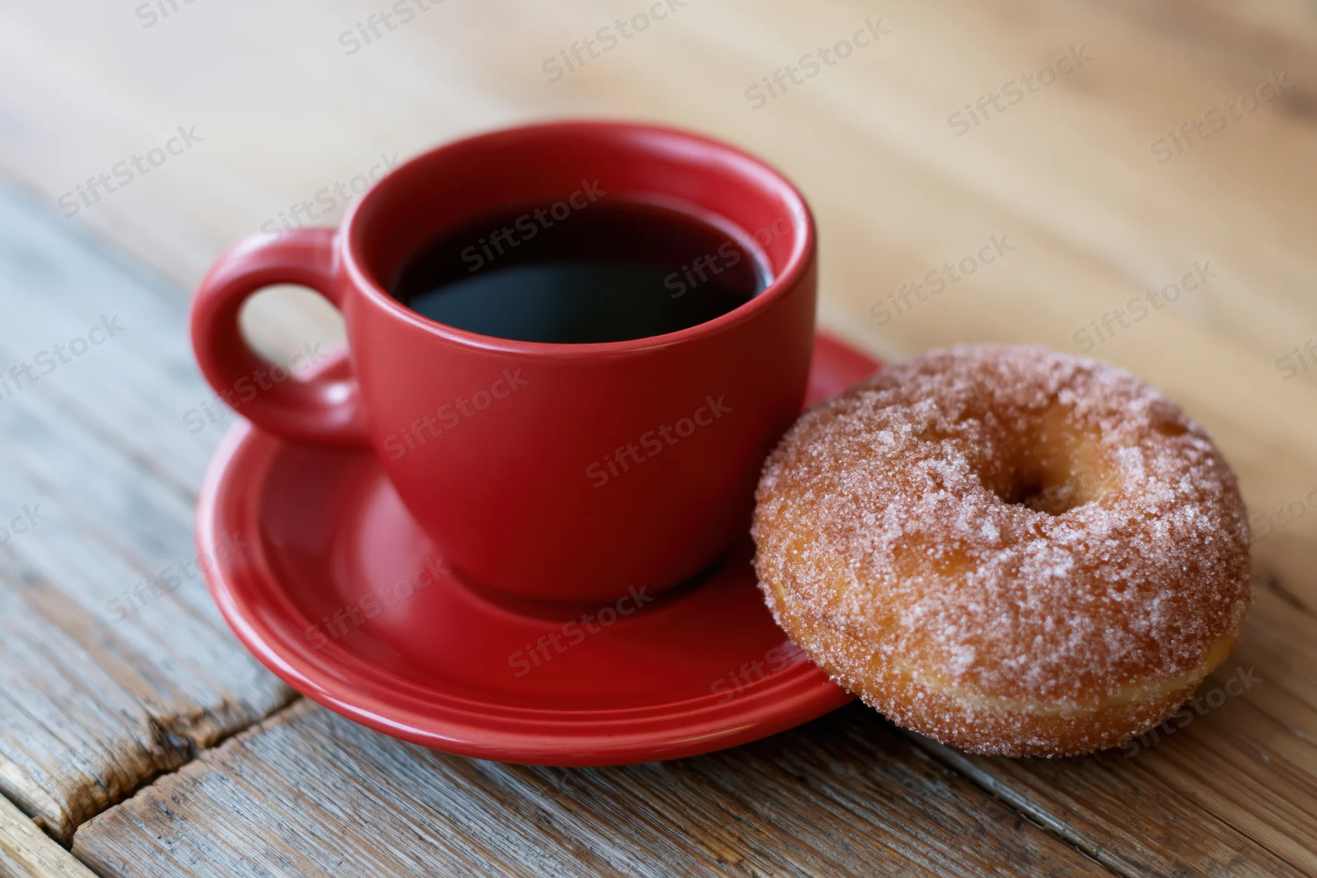 Red ceramic coffee cup with black coffee and a sugar-coated donut on a wooden table