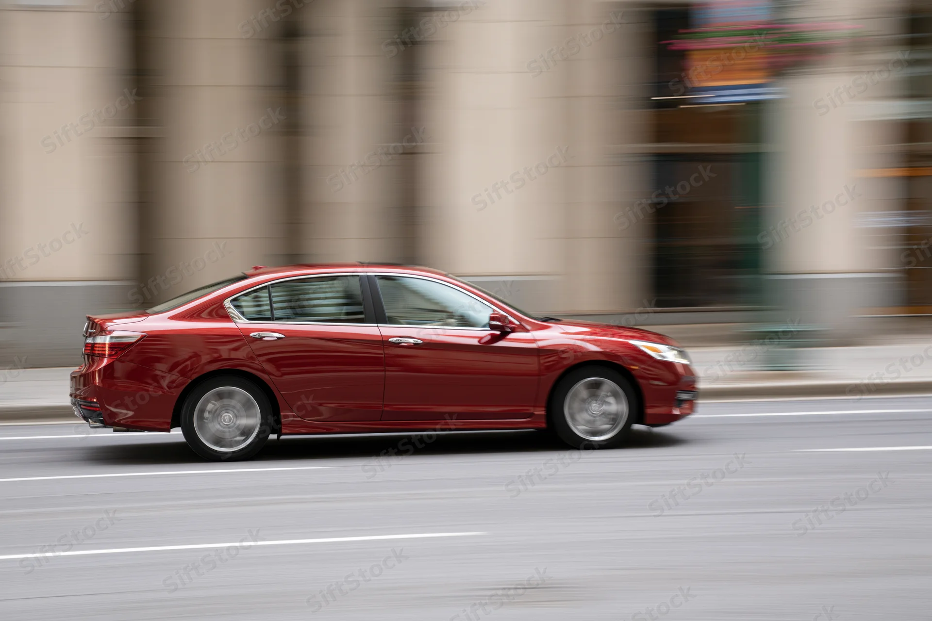 Red compact sedan driving on a city street with motion blur