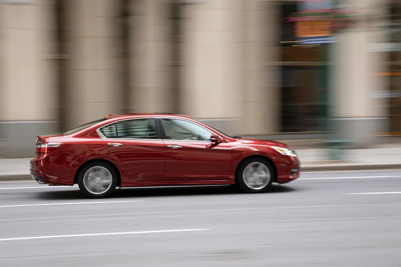 Red compact sedan driving on a city street with motion blur