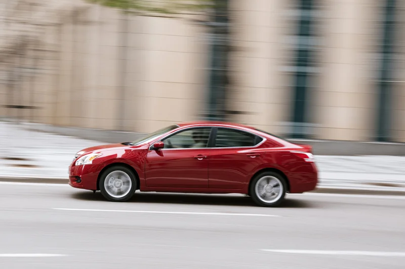 Red compact sedan driving on city street with motion blur