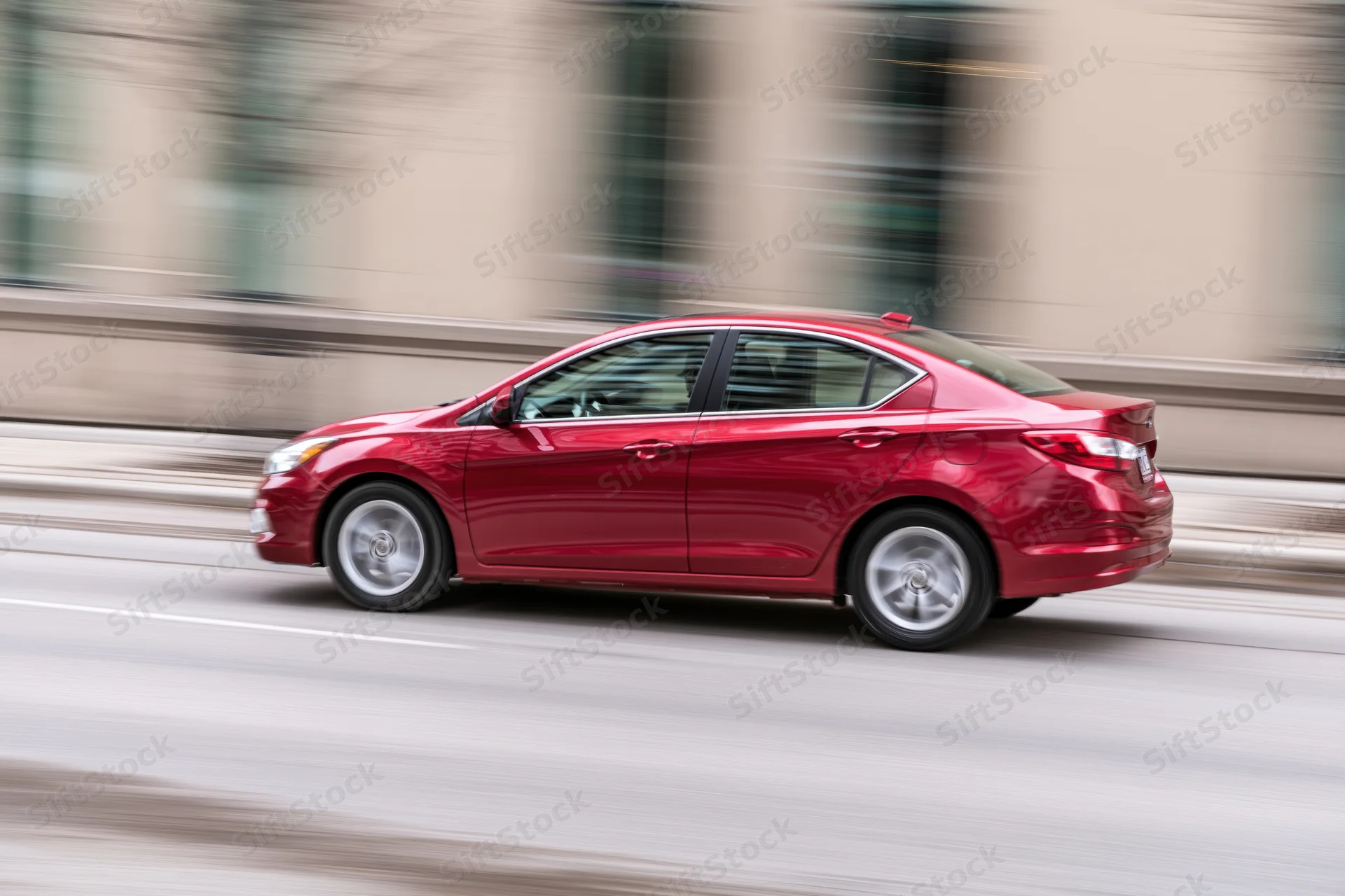 Red compact sedan driving on city street with motion blur