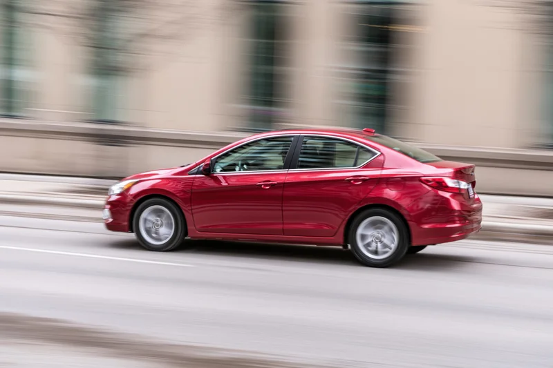 Red compact sedan driving on city street with motion blur