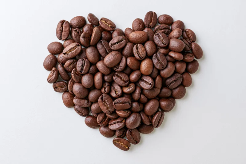 Roasted coffee beans arranged in heart shape on white background