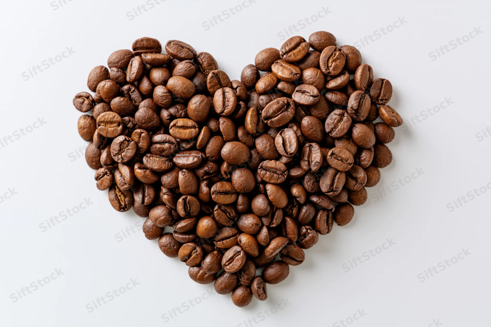 Roasted coffee beans arranged in heart shape on white background