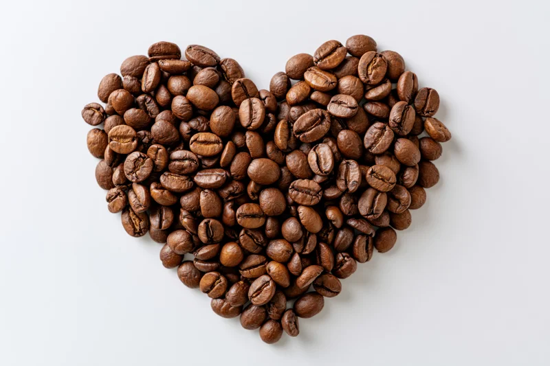 Roasted coffee beans arranged in heart shape on white background