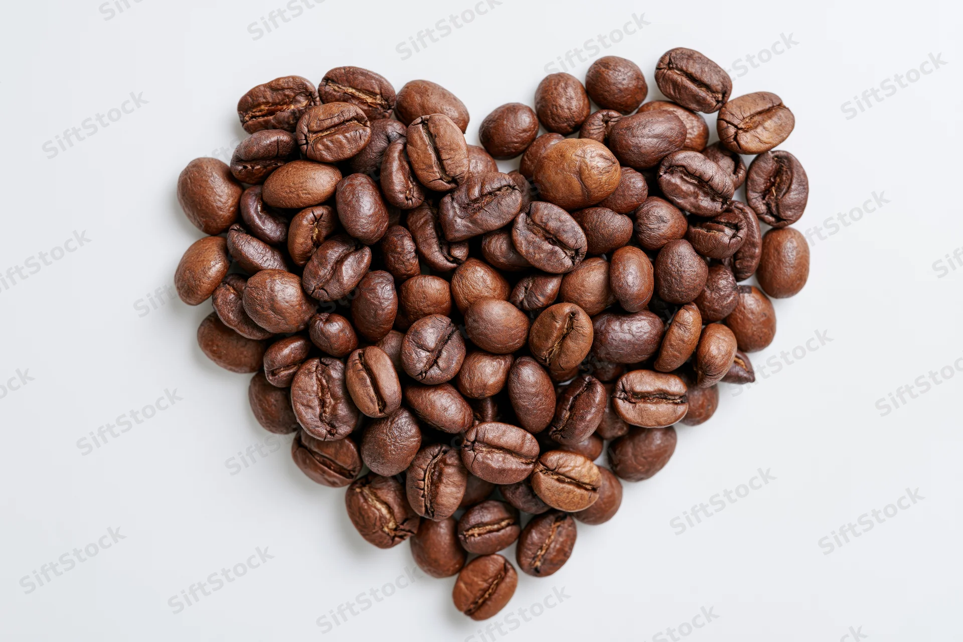 Roasted coffee beans arranged in heart shape on white background