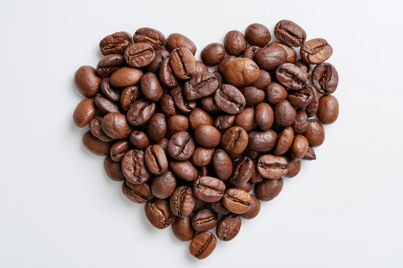 Roasted coffee beans arranged in heart shape on white background