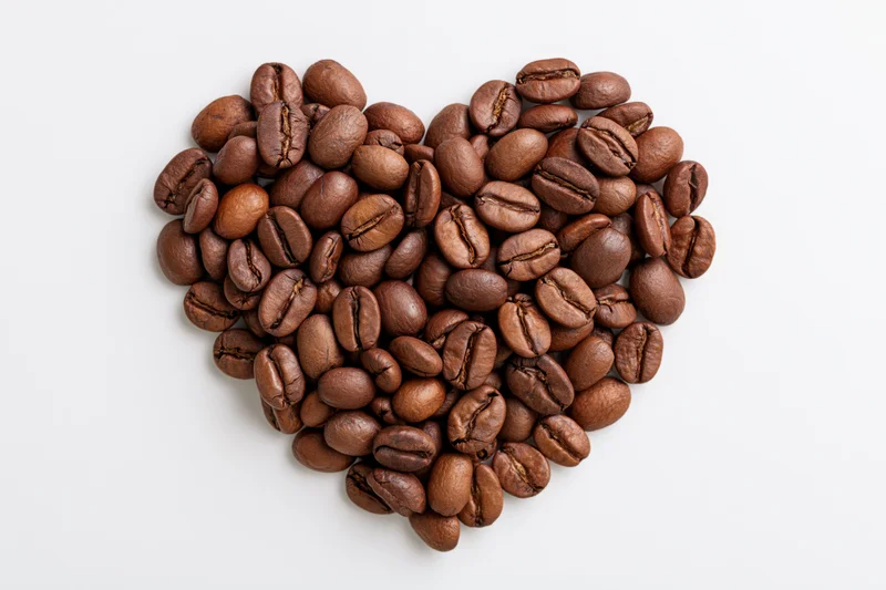 Roasted coffee beans arranged in heart shape on white background