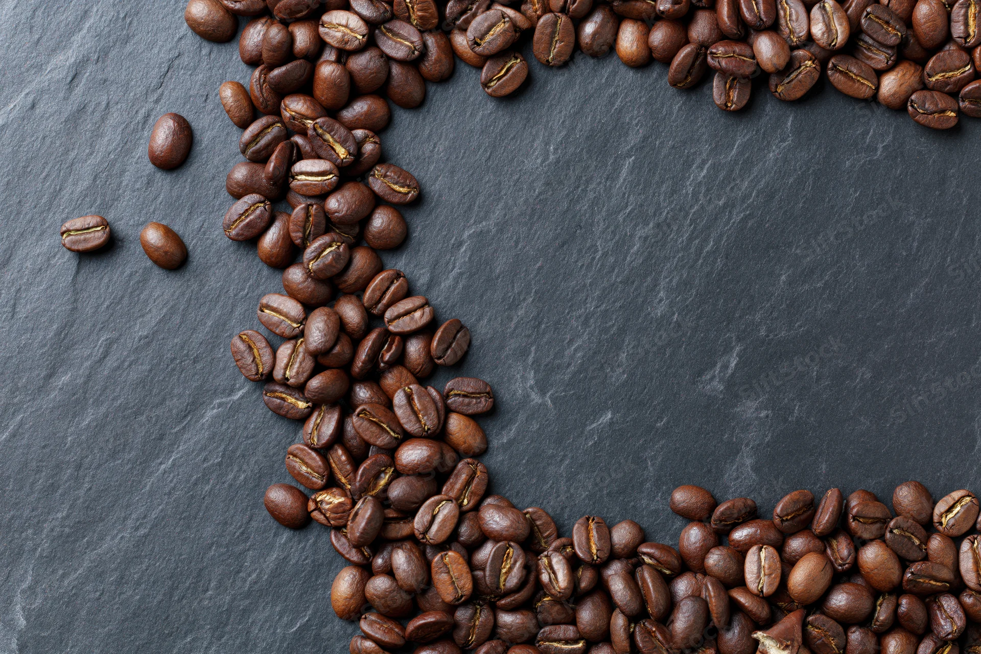 Roasted coffee beans arranged along top and bottom edges on dark slate surface