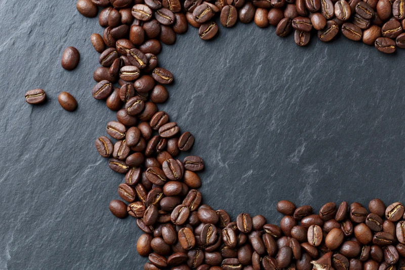 Roasted coffee beans arranged along top and bottom edges on dark slate surface