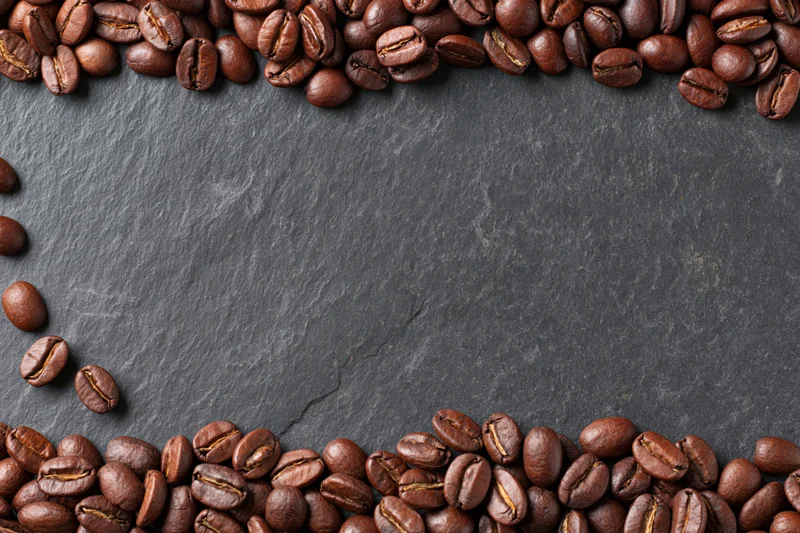 Roasted coffee beans arranged along top and bottom edges on dark slate surface