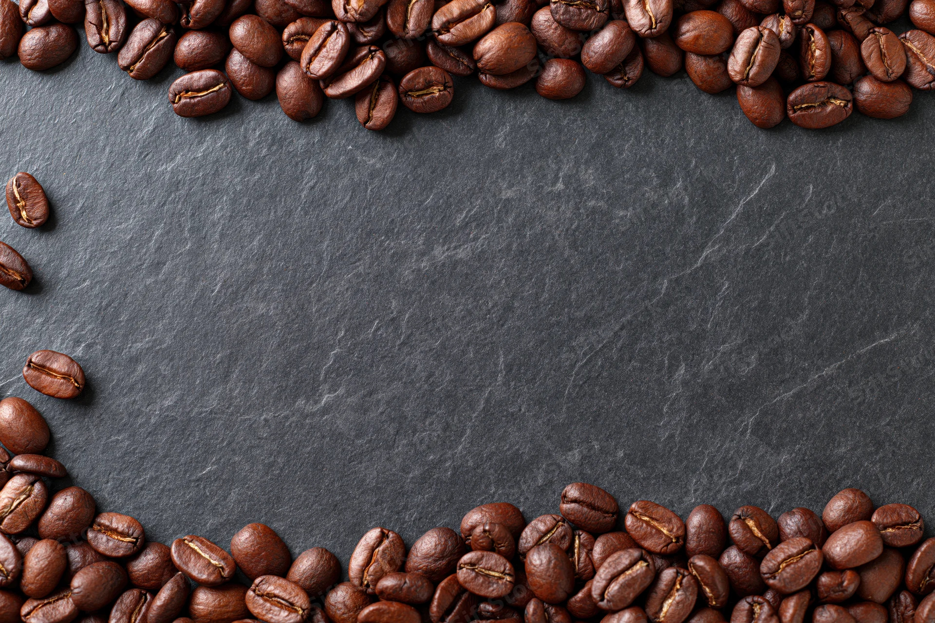Roasted coffee beans arranged along top and bottom edges on dark slate surface
