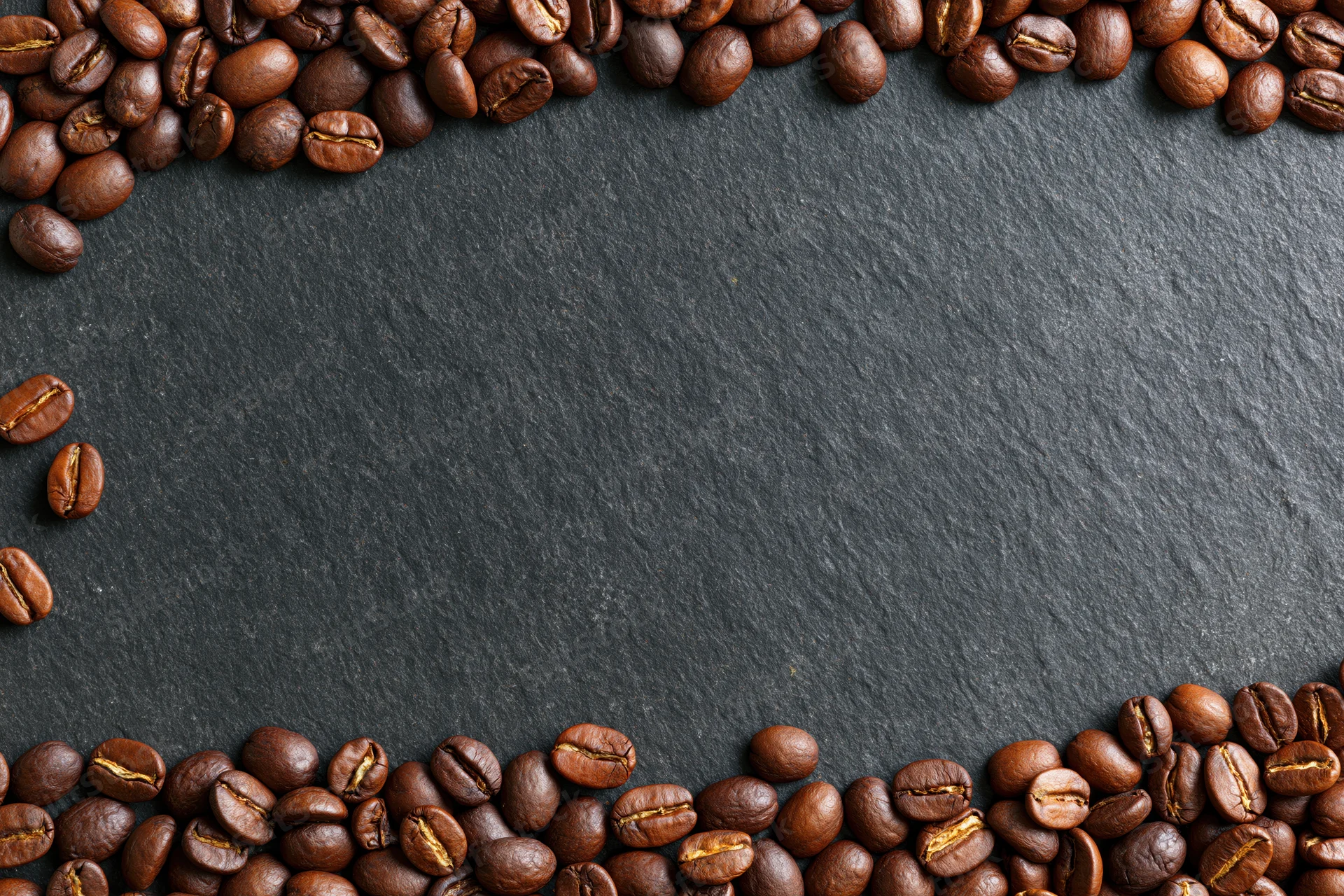 Roasted coffee beans arranged along top and bottom edges on dark slate surface