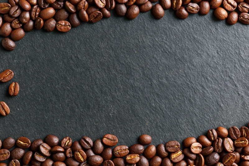 Roasted coffee beans arranged along top and bottom edges on dark slate surface