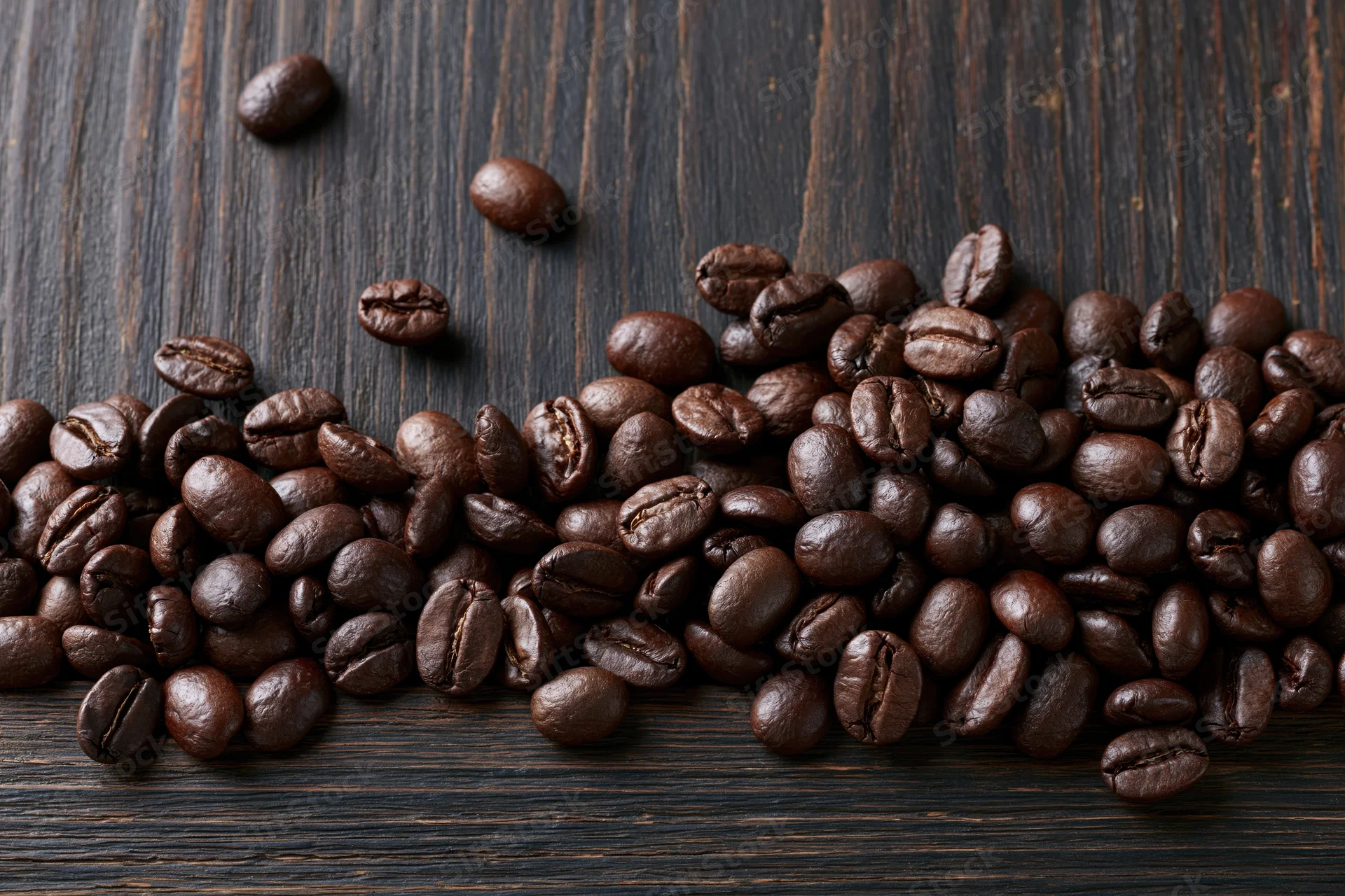 Roasted coffee beans scattered across dark wooden surface