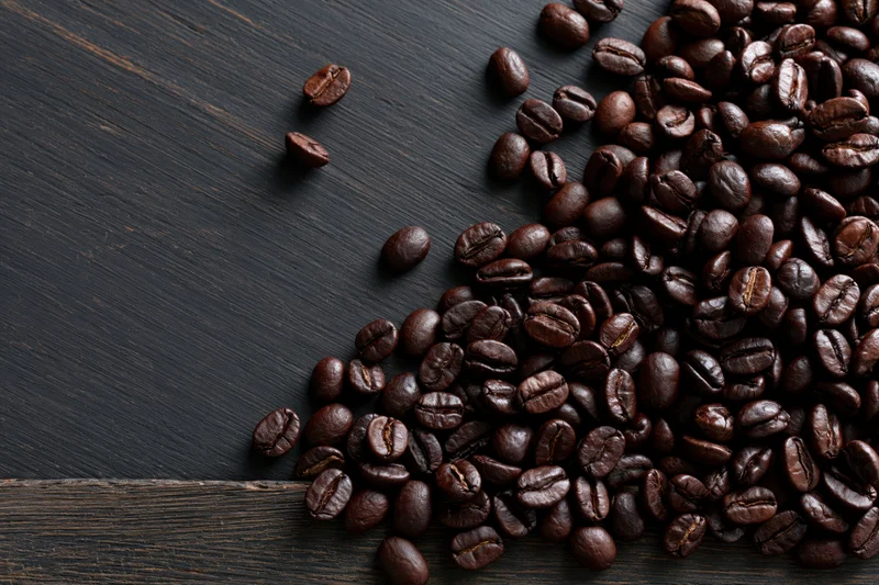 Roasted coffee beans scattered across the bottom edge of a dark wooden surface