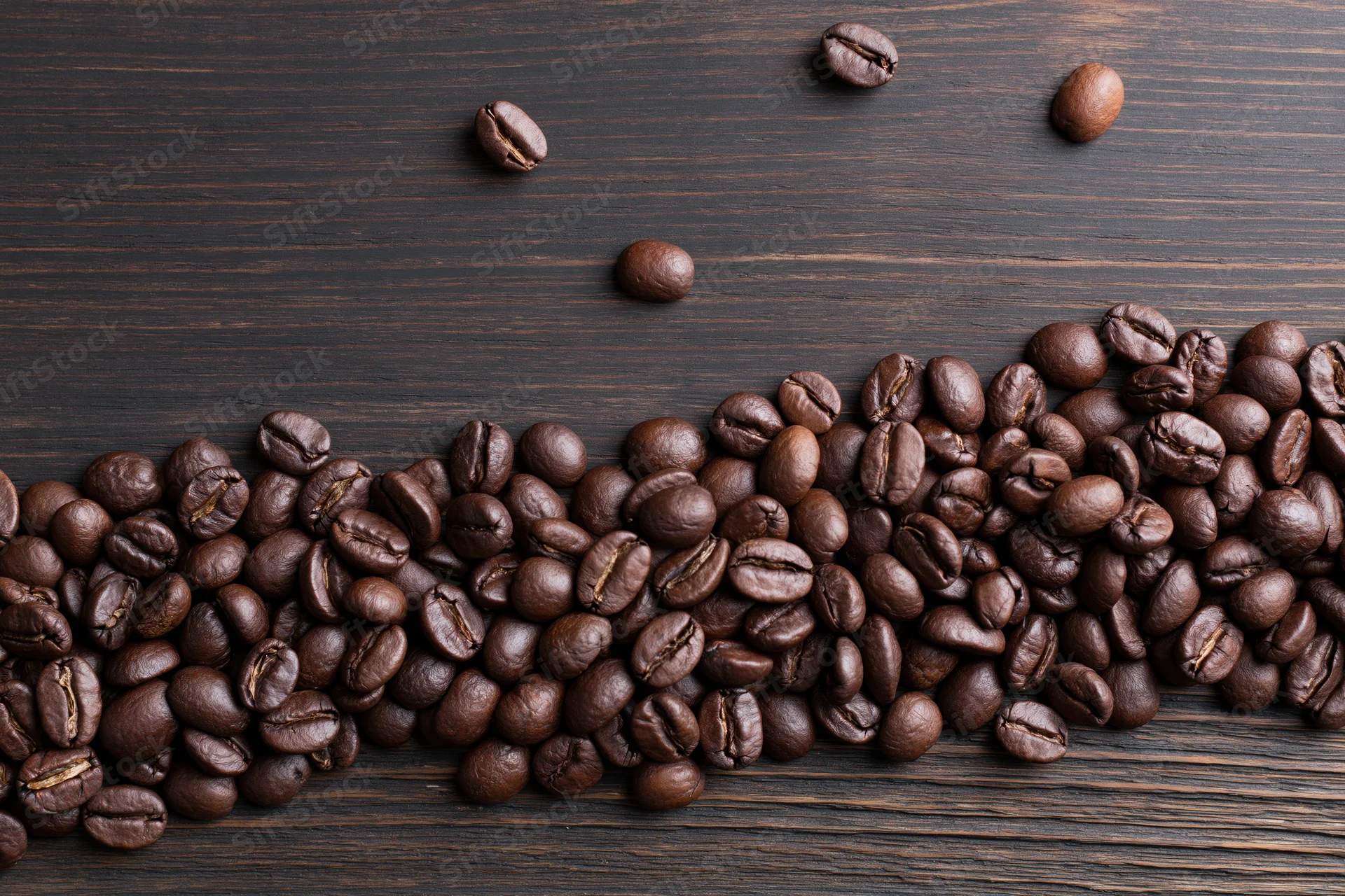 Roasted coffee beans scattered across the bottom edge of a dark wooden surface