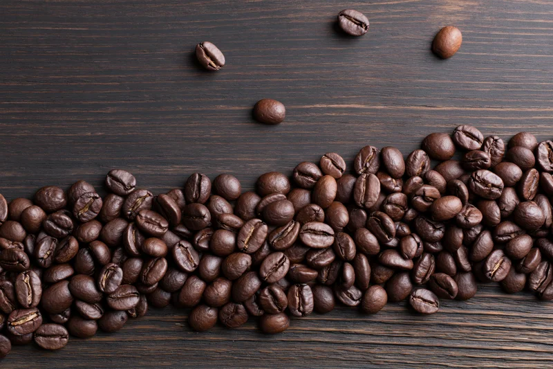 Roasted coffee beans scattered across the bottom edge of a dark wooden surface