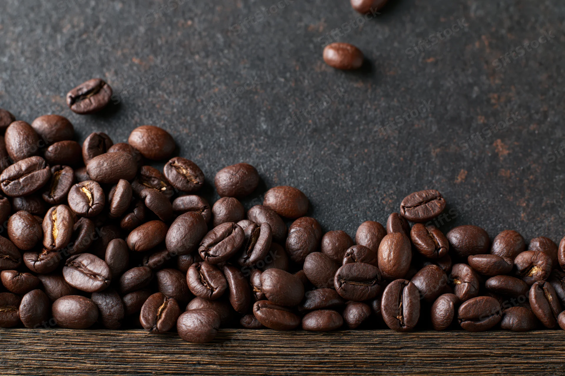 Roasted coffee beans scattered along the bottom edge on a dark textured surface