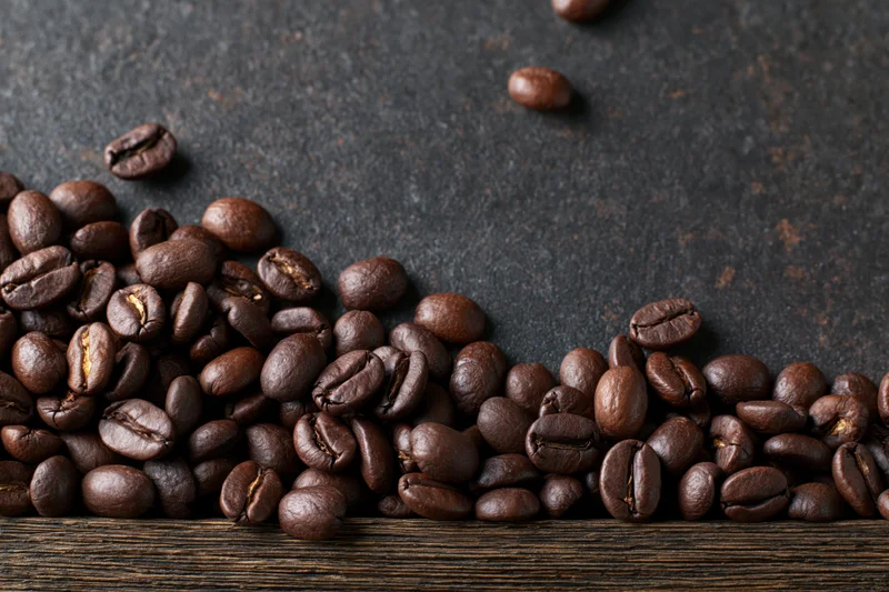 Roasted coffee beans scattered along the bottom edge on a dark textured surface
