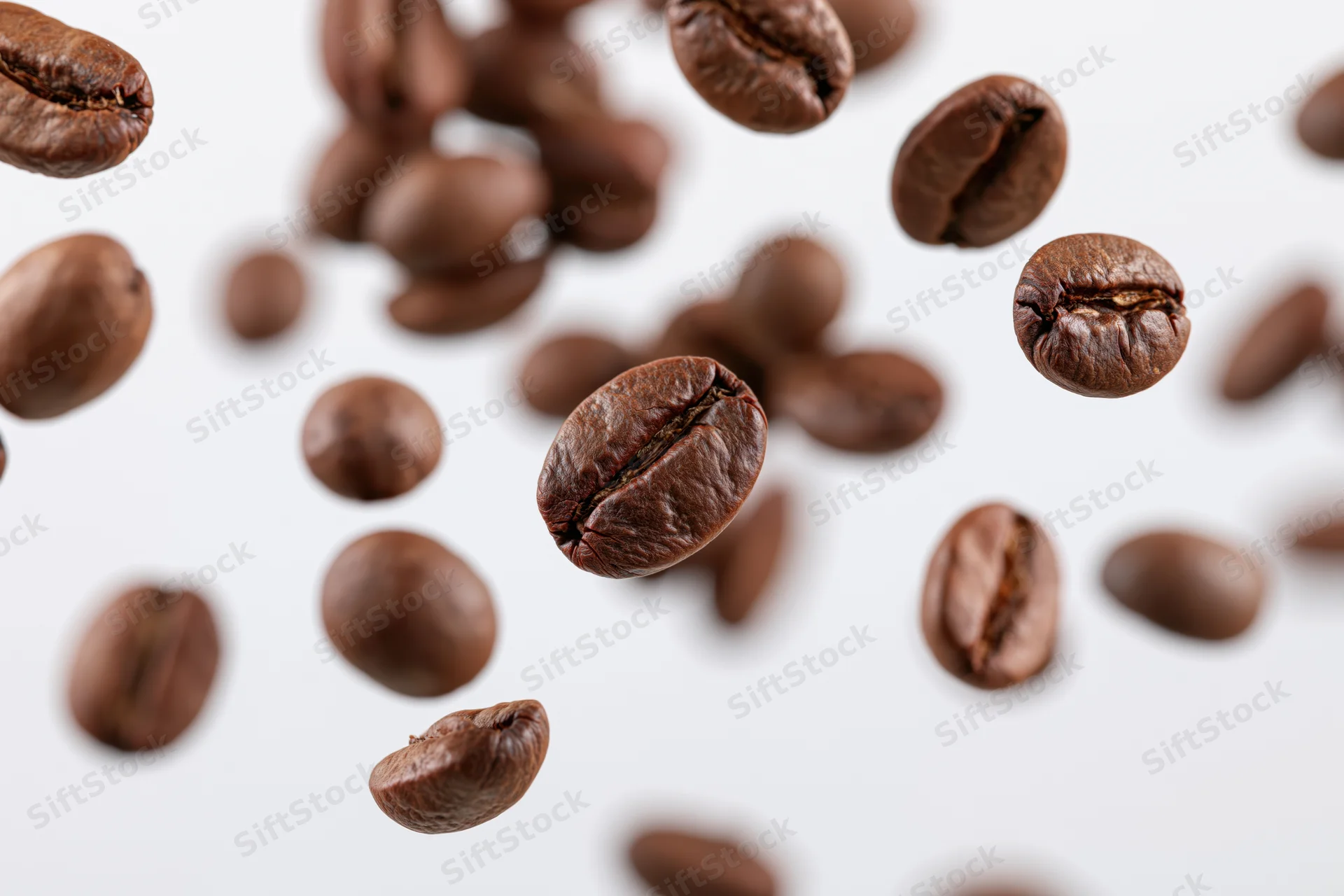 Roasted coffee beans falling midair scattered against white background