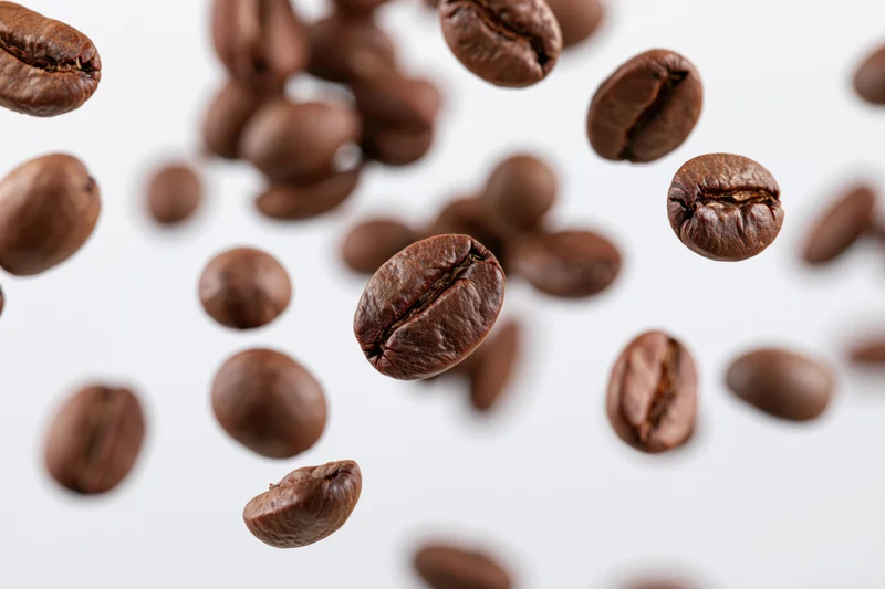 Roasted coffee beans falling midair scattered against white background