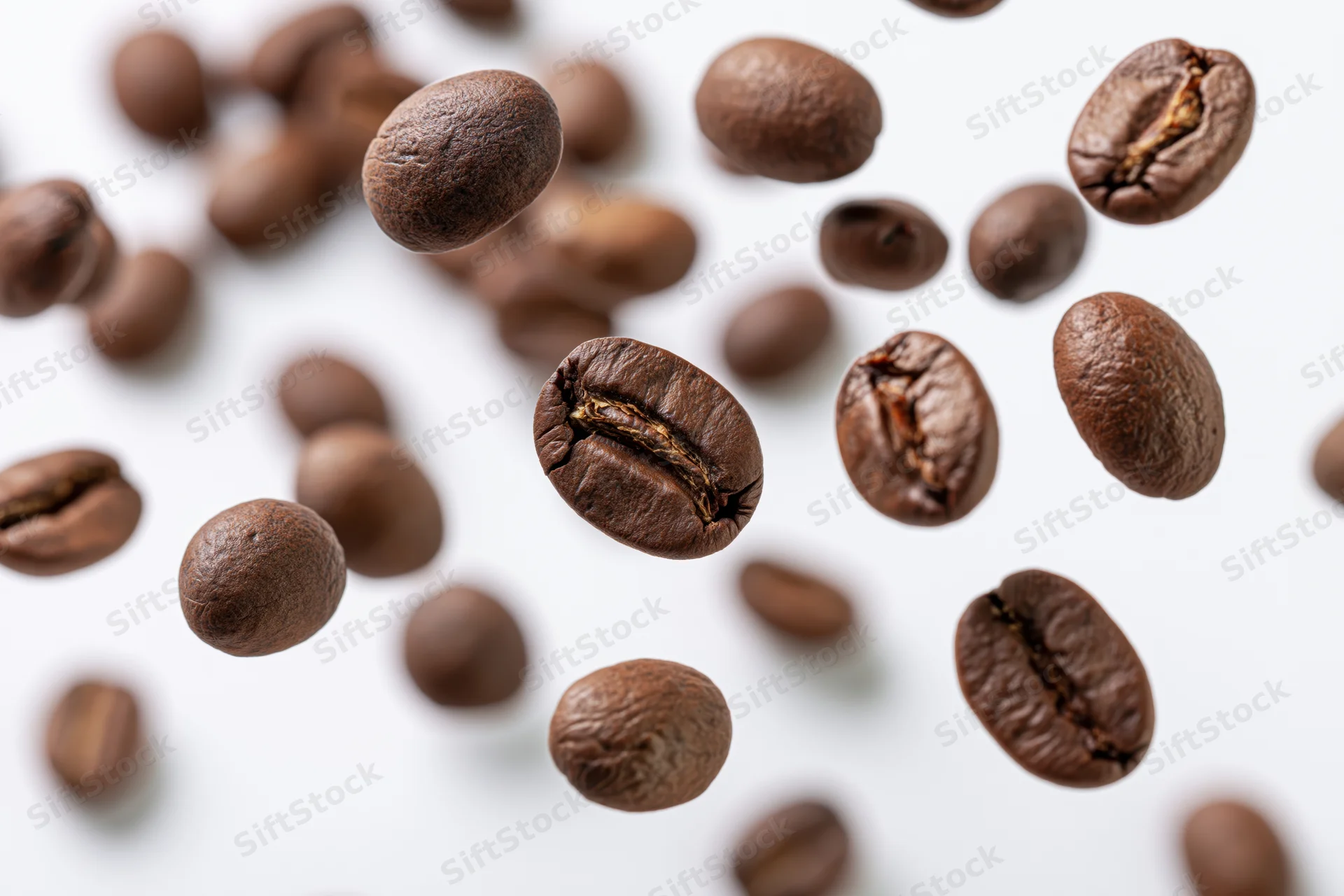Roasted coffee beans falling midair scattered over white background