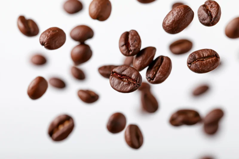 Roasted coffee beans falling midair scattered against white background