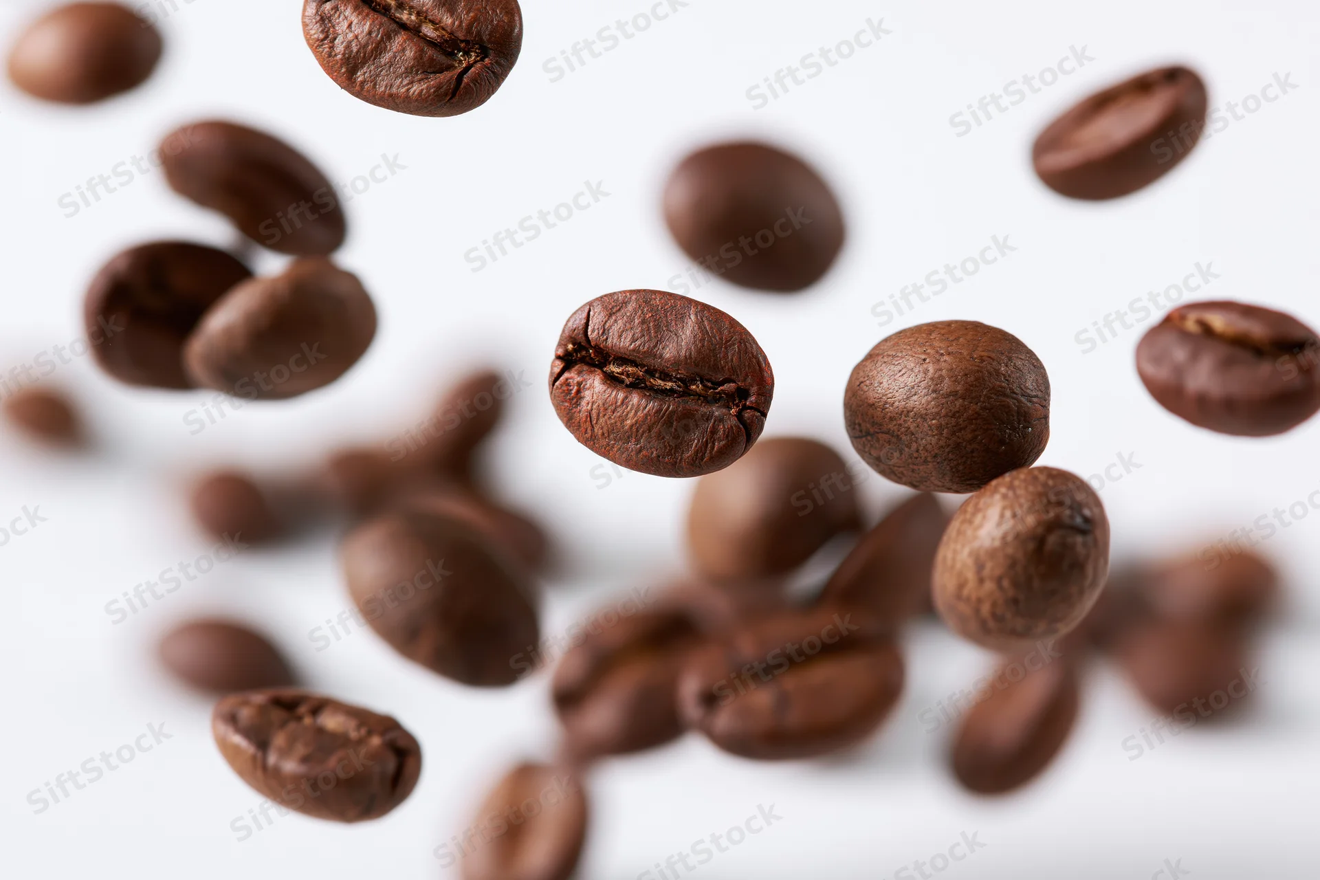Roasted coffee beans falling midair against white background