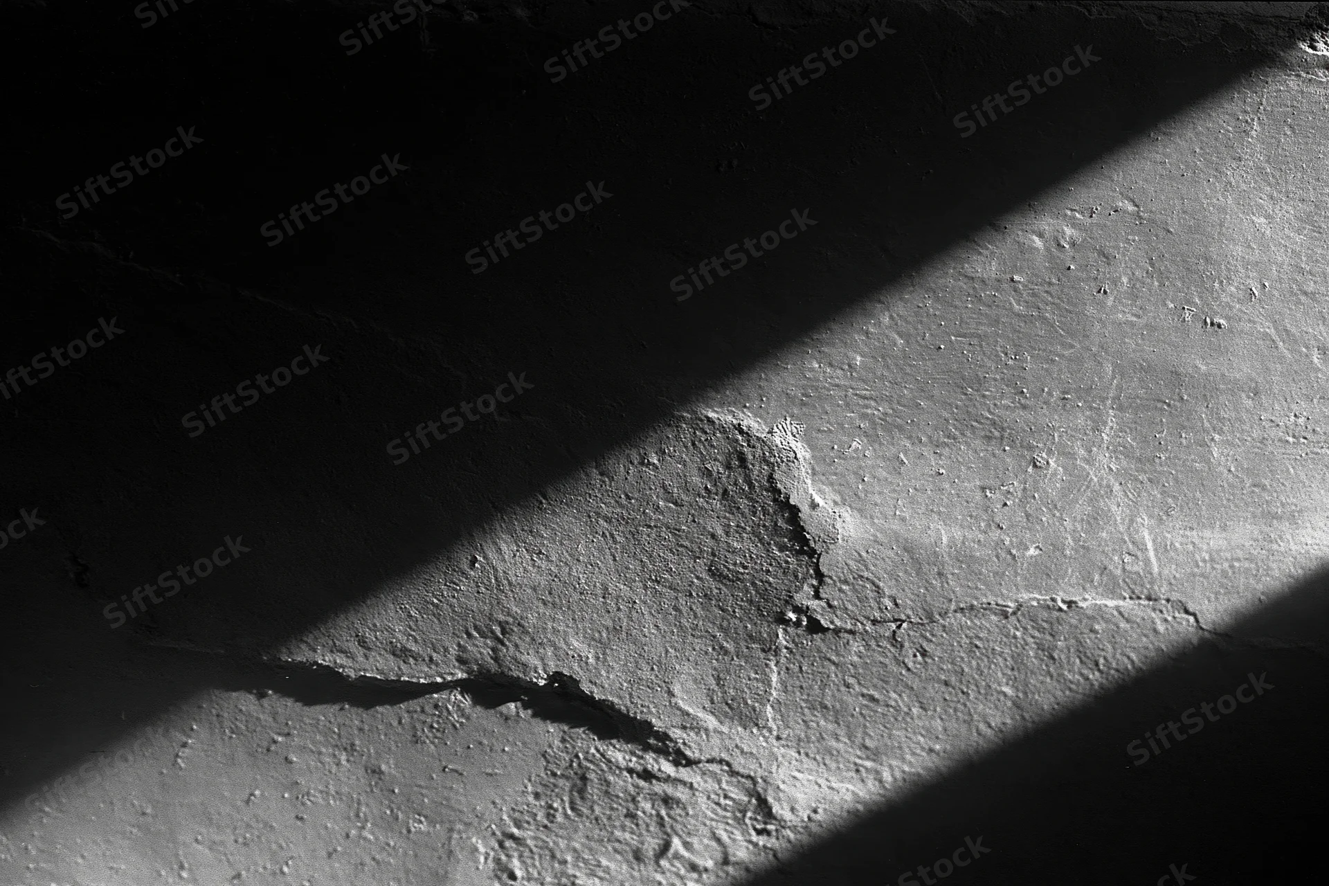 Rough concrete wall with cracks and peeling texture under diagonal shadow
