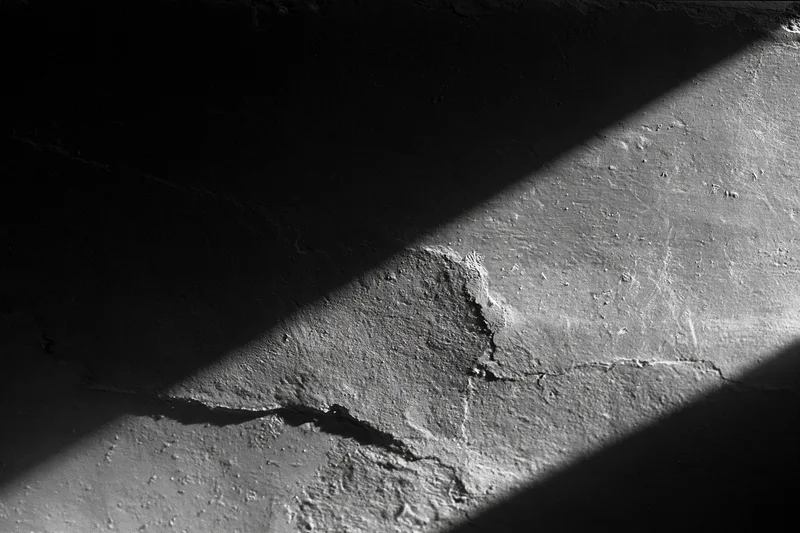 Rough concrete wall with cracks and peeling texture under diagonal shadow