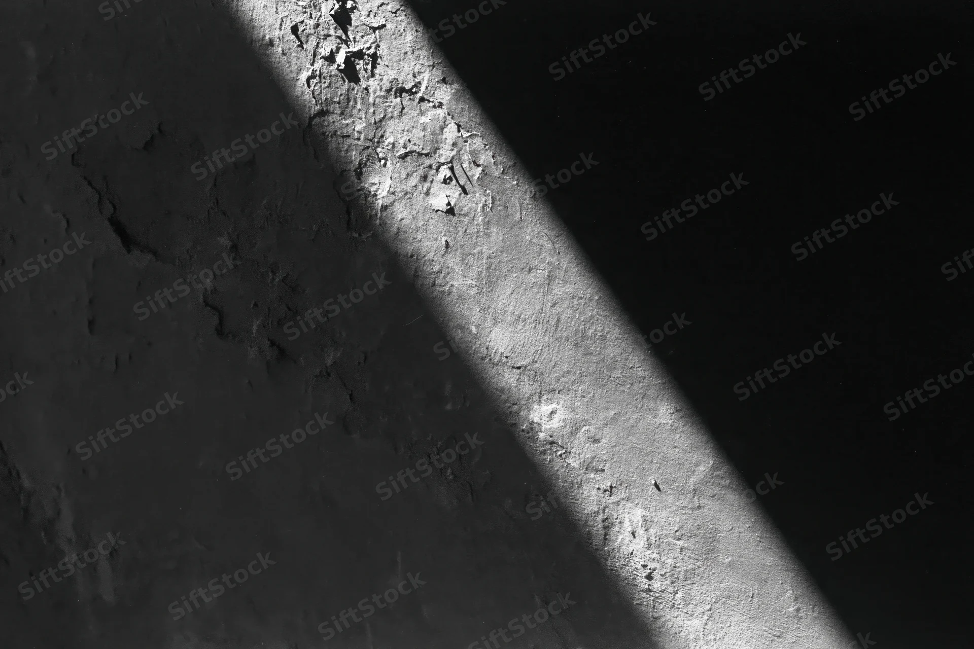 Diagonal light stripe across rough peeling concrete wall surface