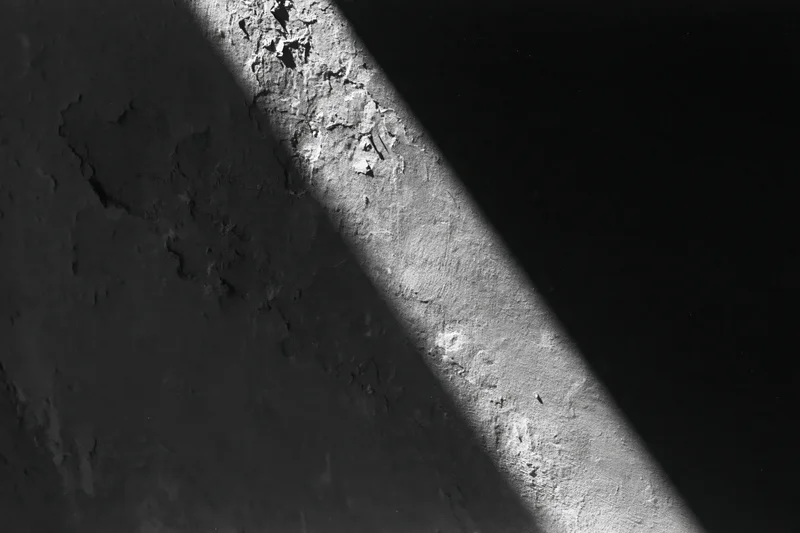 Diagonal light stripe across rough peeling concrete wall surface