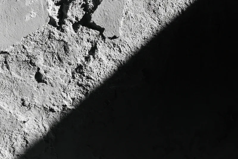 Rough concrete wall with peeling texture and shadowed surface