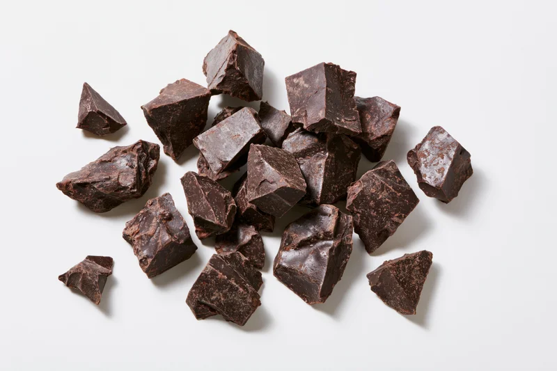Broken dark chocolate chunks scattered loosely on white background