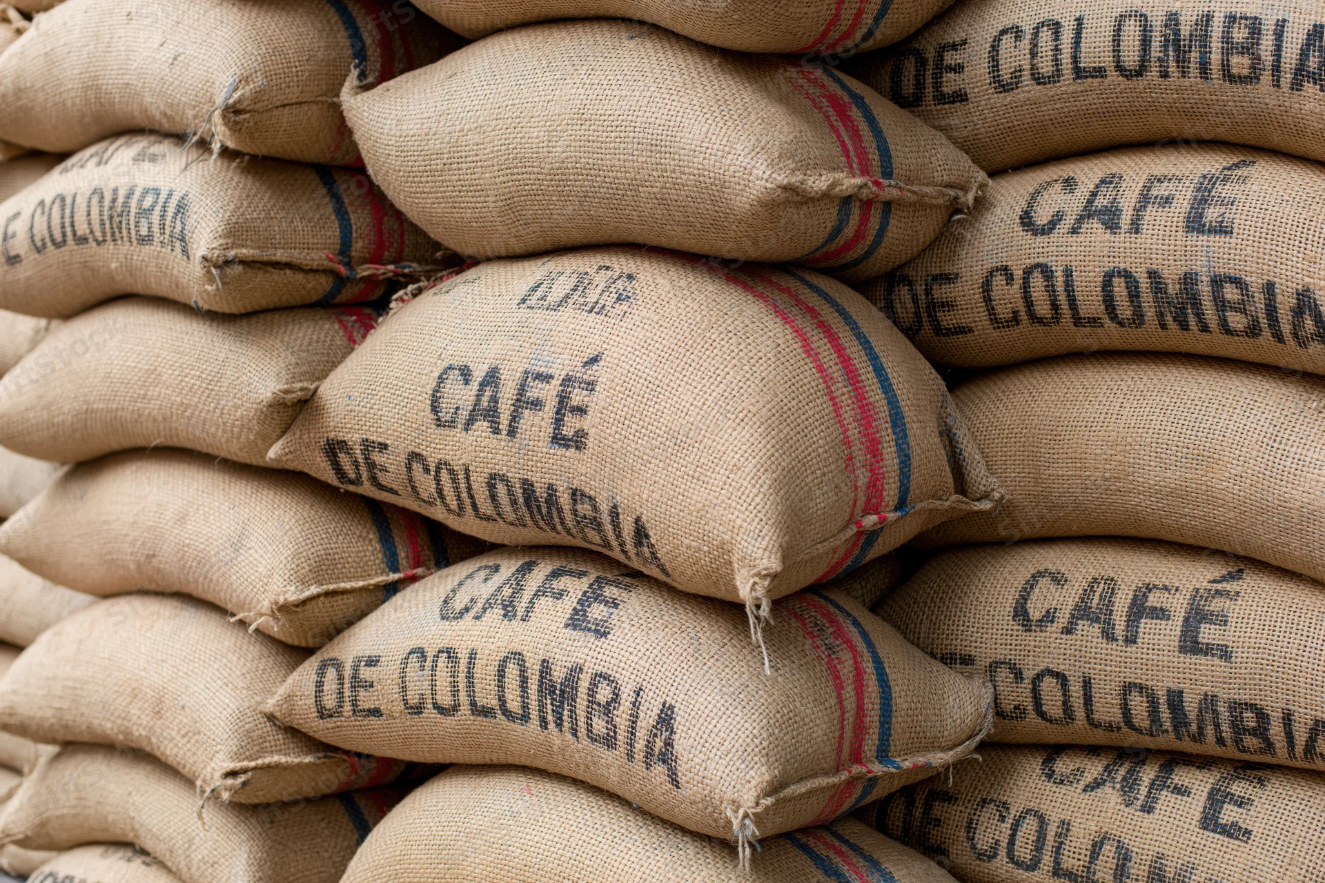 Stacked burlap coffee sacks labeled cafe de colombia in a warehouse