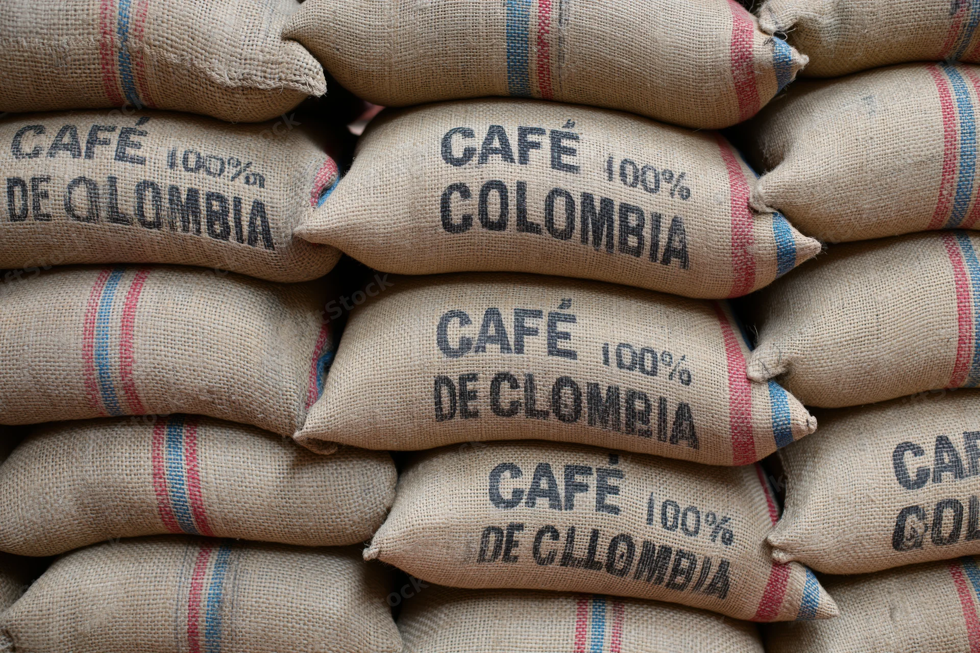 Stacked burlap coffee sacks labeled cafe 100% colombia in a warehouse storage area