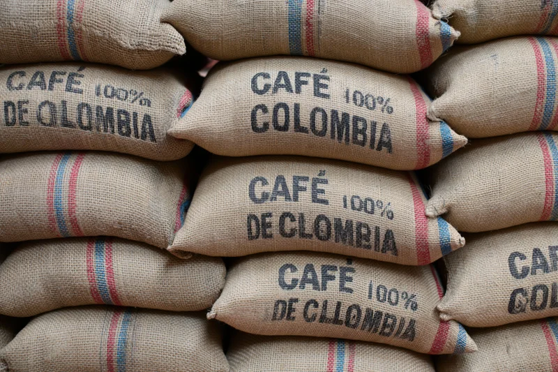 Stacked burlap coffee sacks labeled cafe 100% colombia in a warehouse storage area