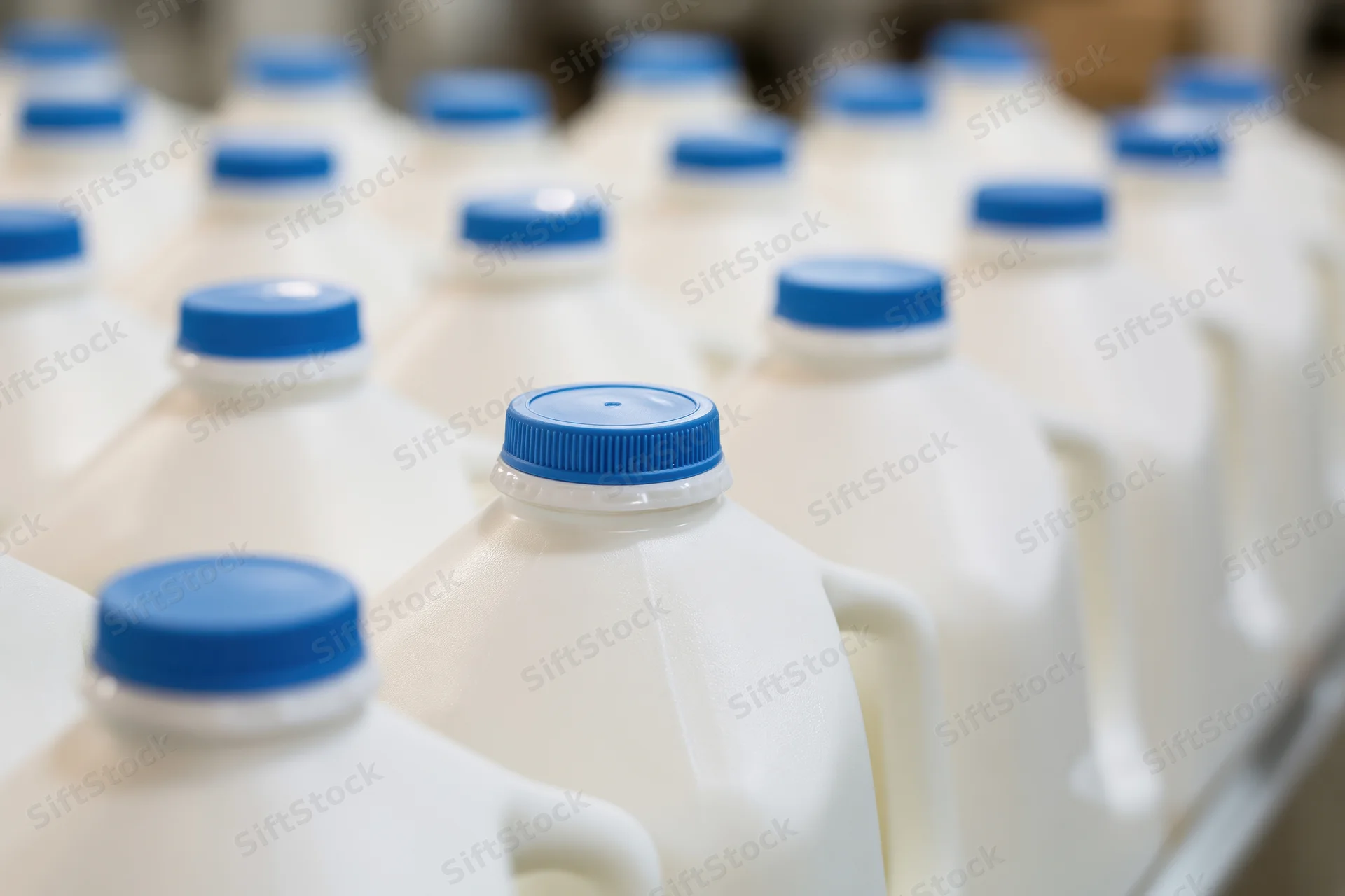 Rows of white plastic milk jugs with blue caps arranged on a production line
