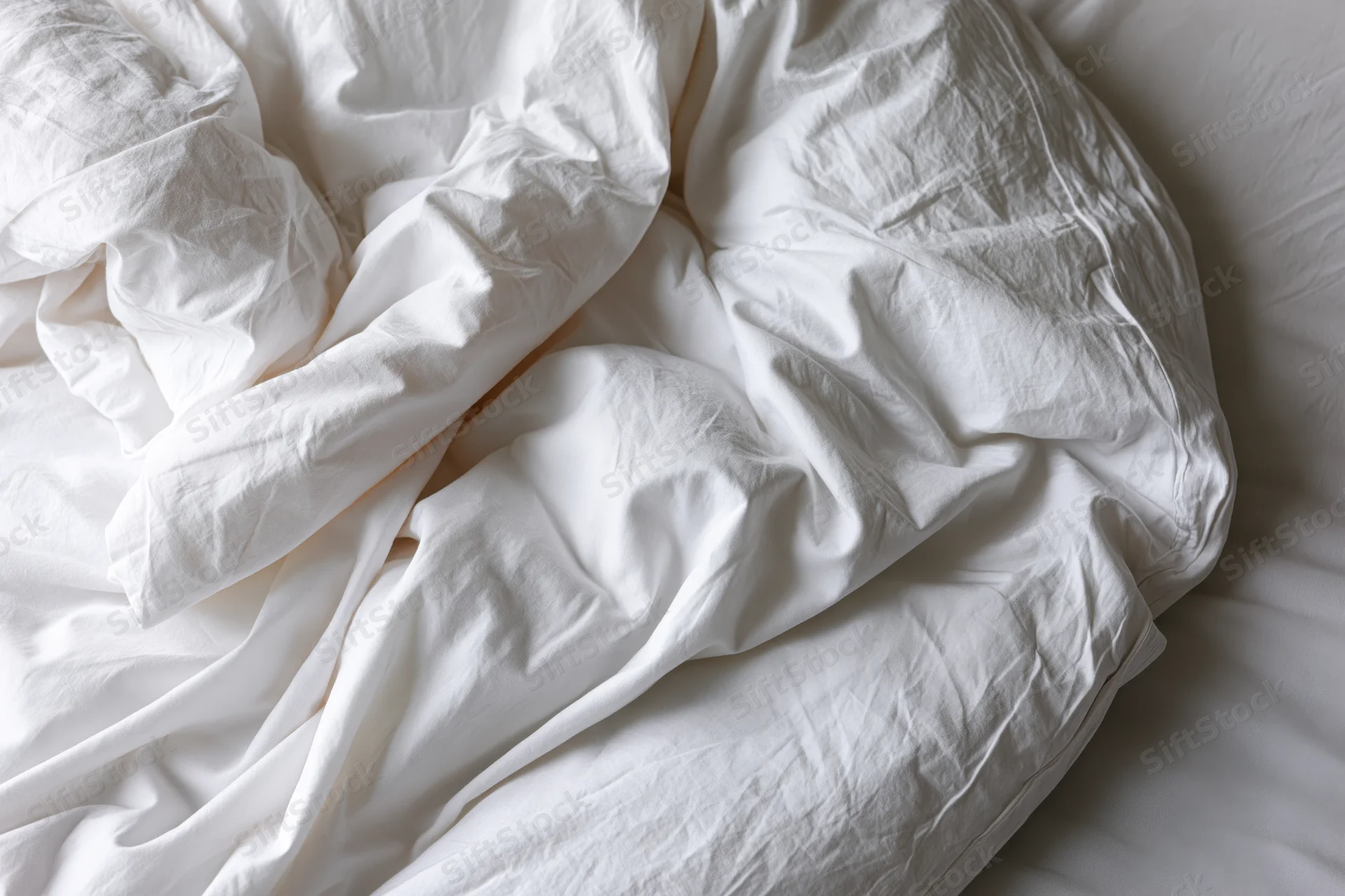 Rumpled white duvet and sheet bunched on a bed in a bedroom