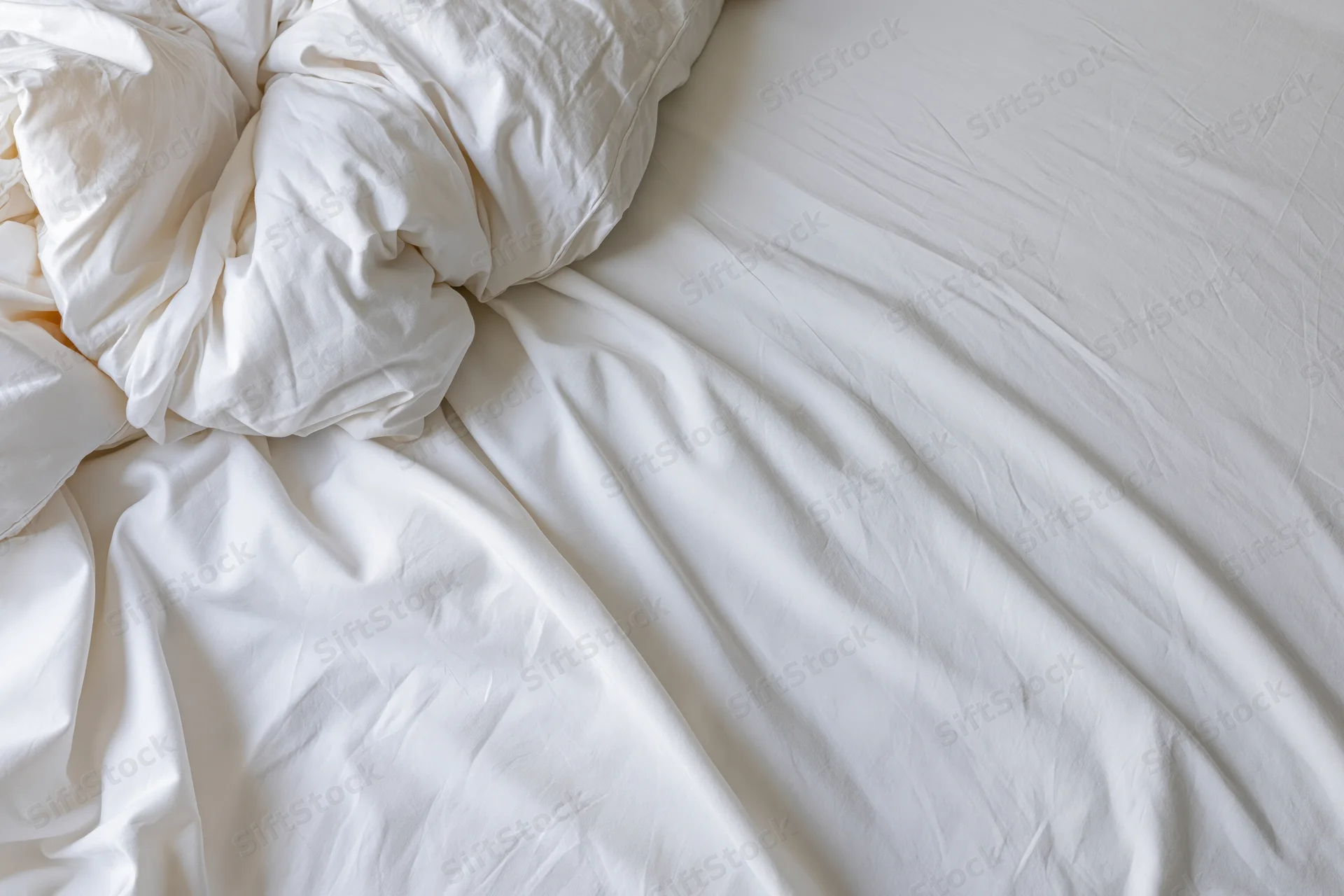 Rumpled white bedsheet and duvet bunched toward the upper-left corner of an unmade bed