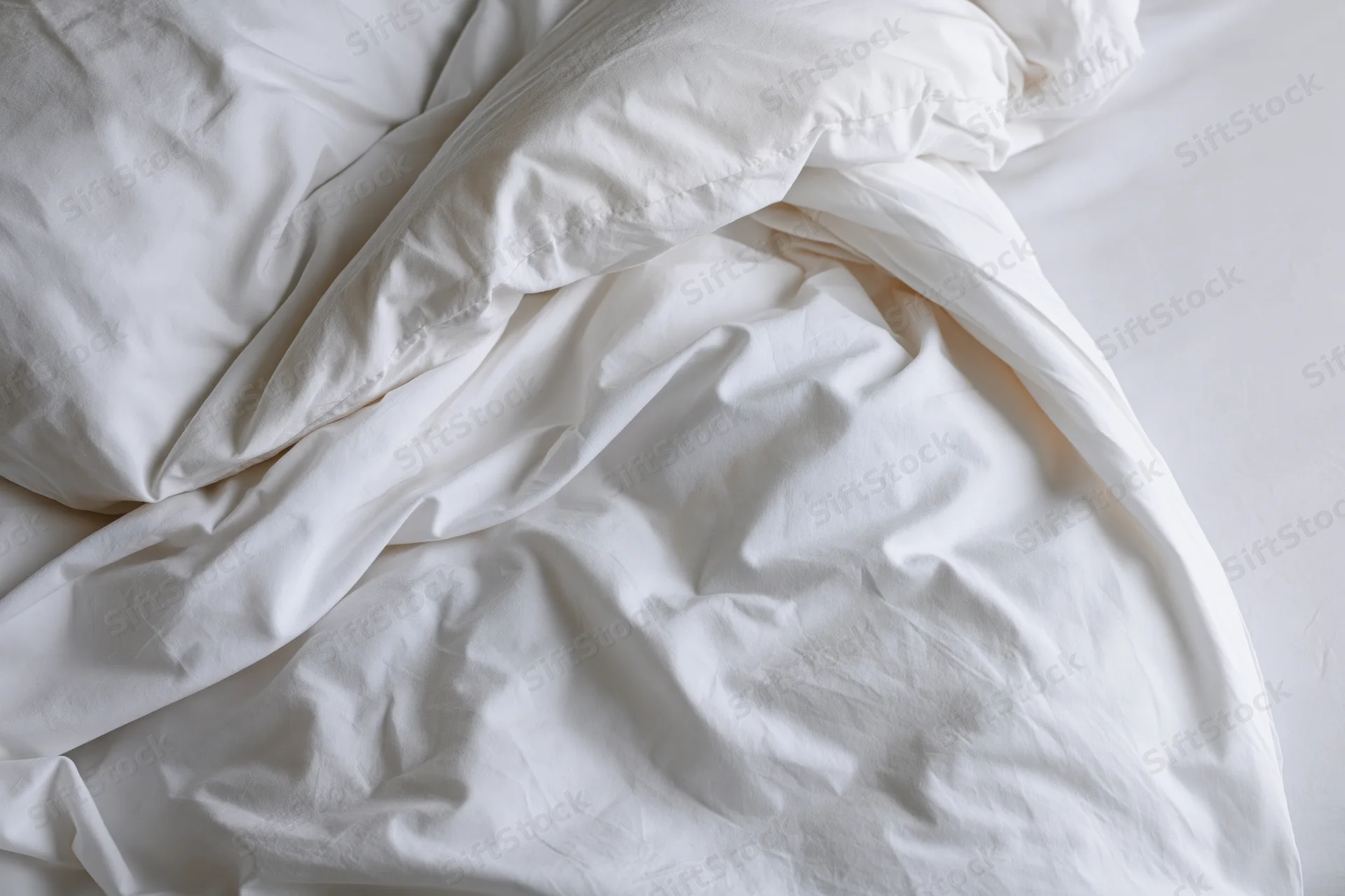 Rumpled white bedding and duvet bunched toward the upper-left corner of the bed
