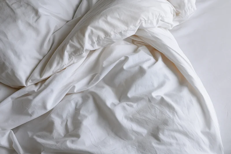 Rumpled white bedding and duvet bunched toward the upper-left corner of the bed