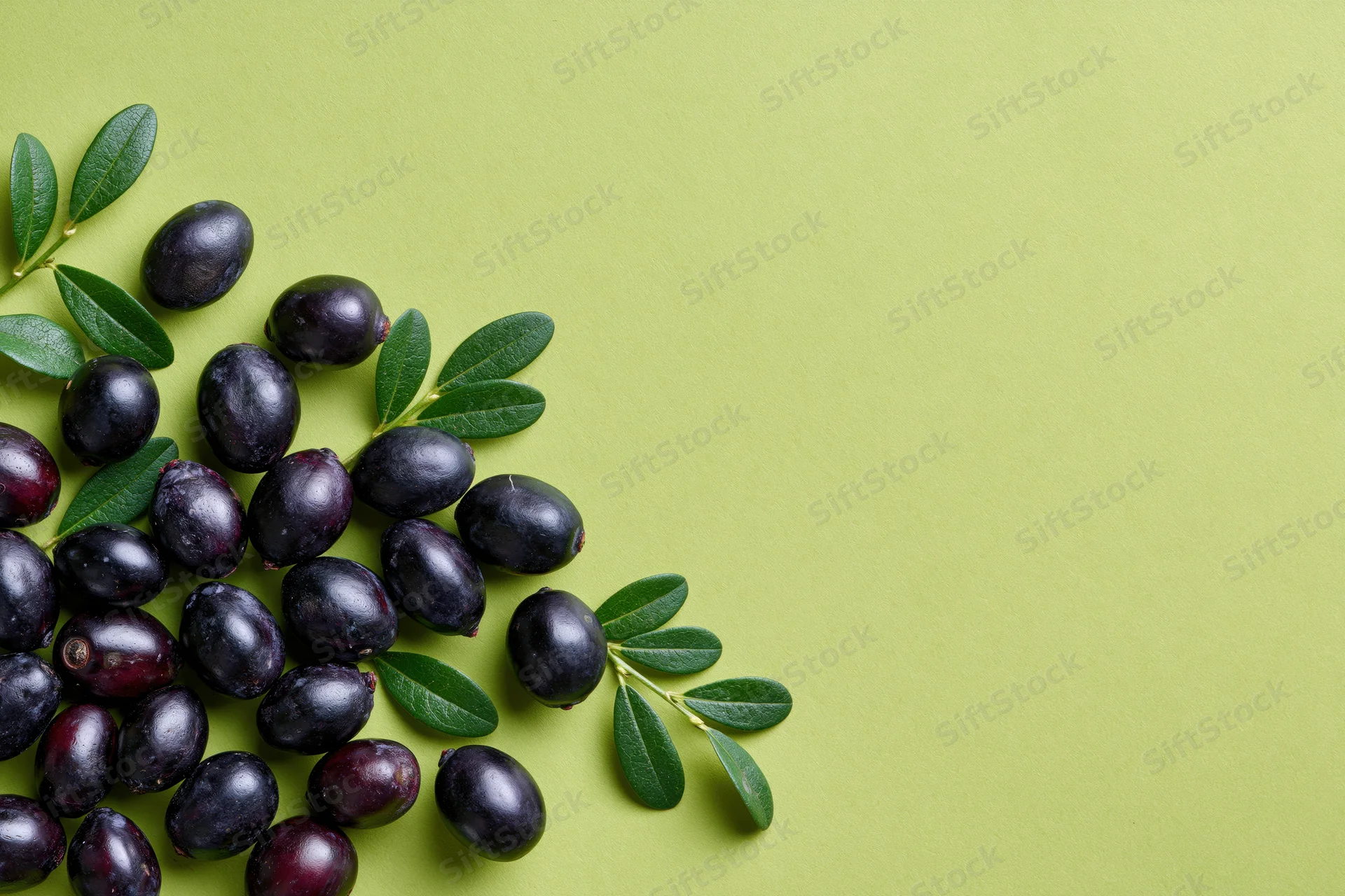 Acai berries and green leaves arranged in a cluster on a green surface with copyspace