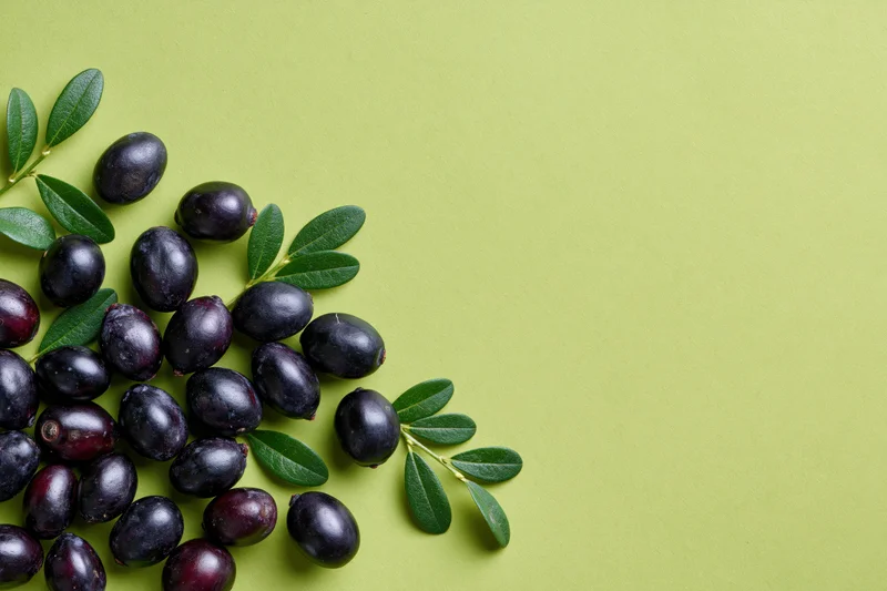 Acai berries and green leaves arranged in a cluster on a green surface with copyspace